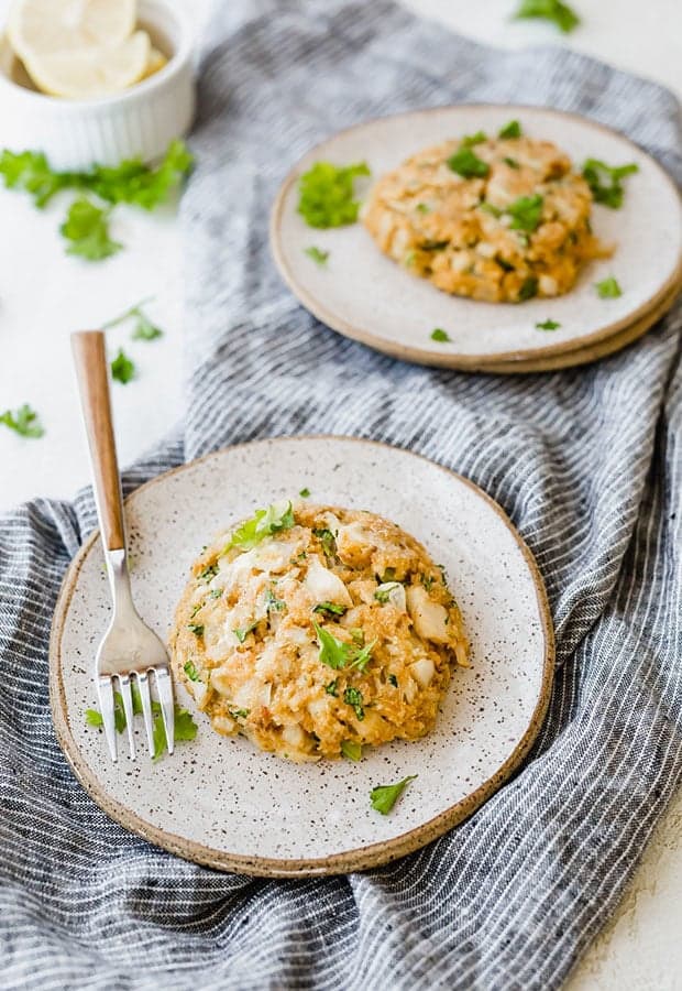 Tilapia cake on a small plate topped with fresh parsley and a fork resting along side the fish cake.