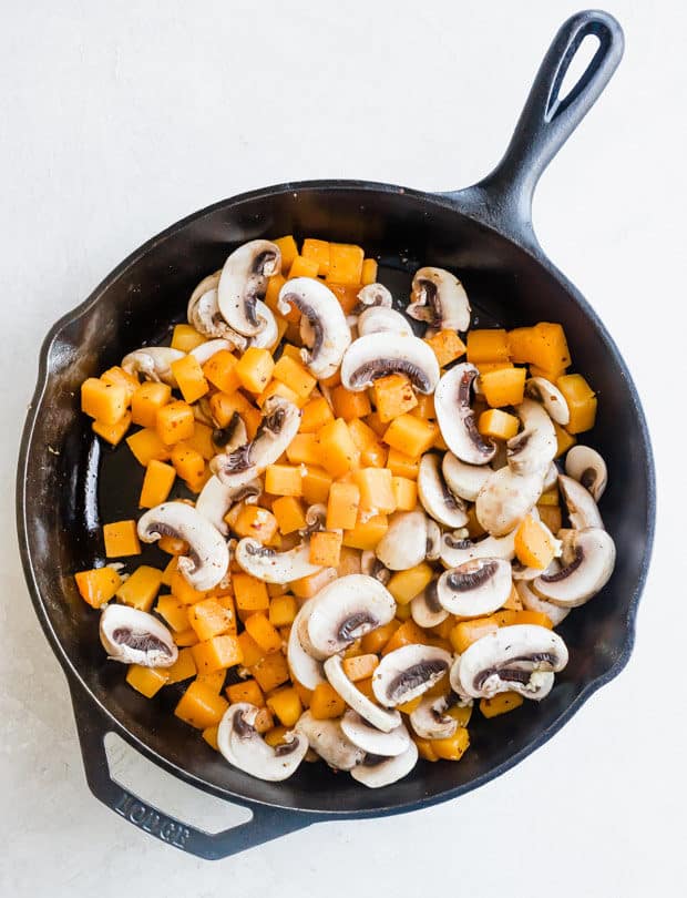 A black skillet with diced butternut squash and sliced mushrooms.