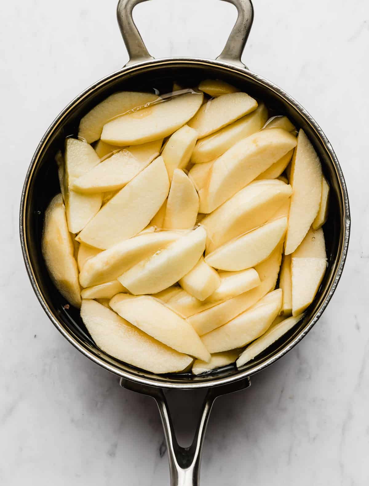 Peeled and sliced apples in a water filled saucepan.