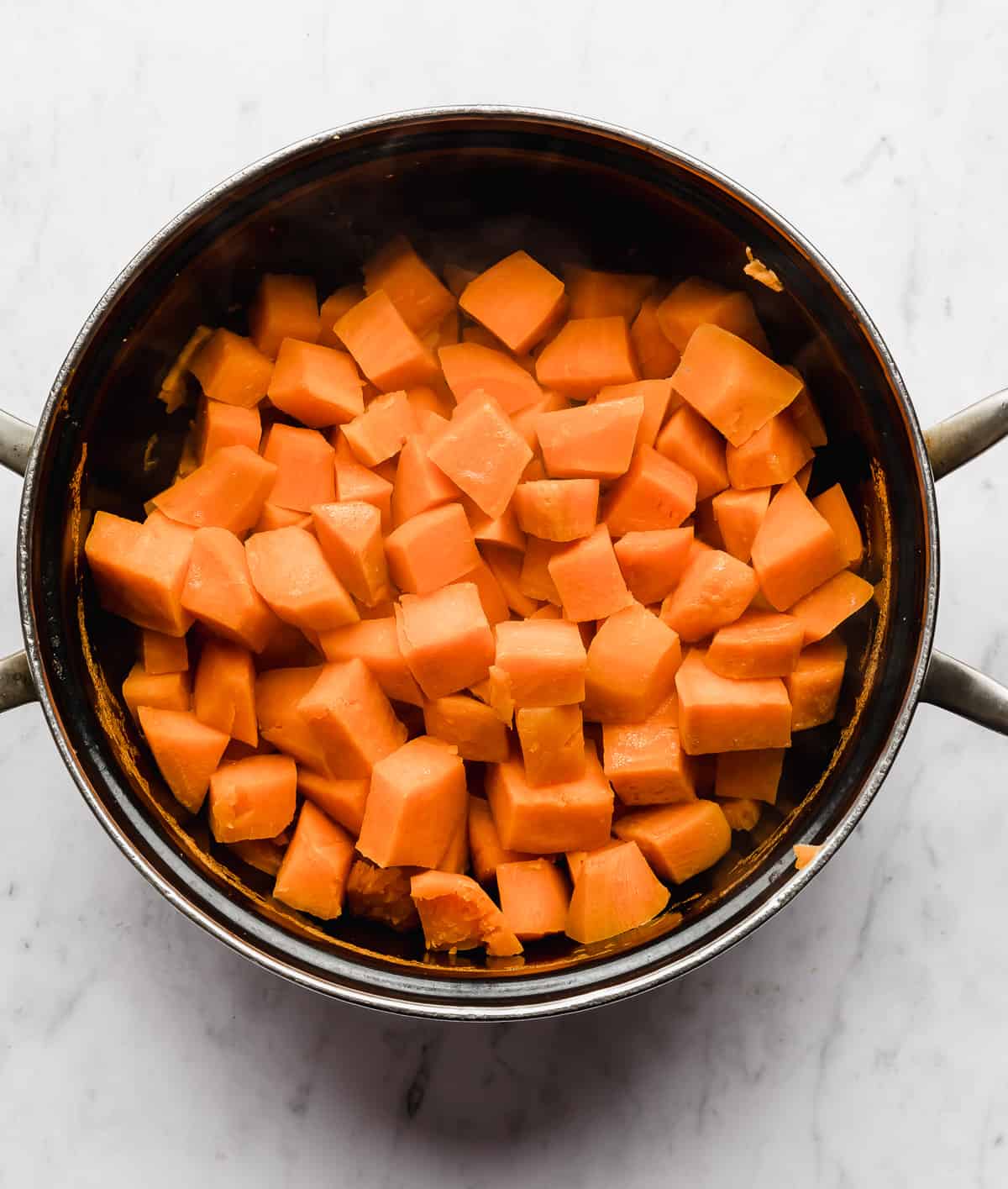A black pot full of cooked, cubed, sweet potatoes.
