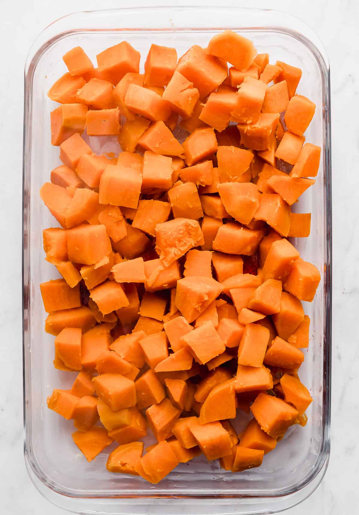 Cubed sweet potatoes in a glass casserole dish.