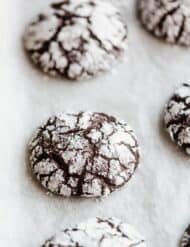 Freshly baked easy chocolate crinkle cookies on a parchment lined baking sheet.