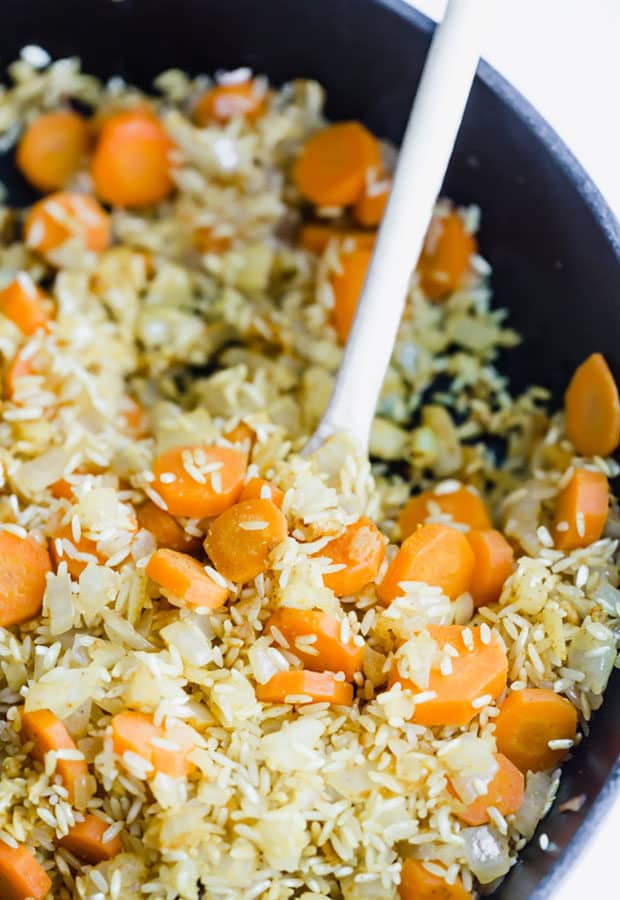 Chopped carrots and white rice in a black cast iron skillet.