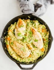 Overhead photo of a cast iron skillet with cooked curry chicken and rice with peas and carrots.