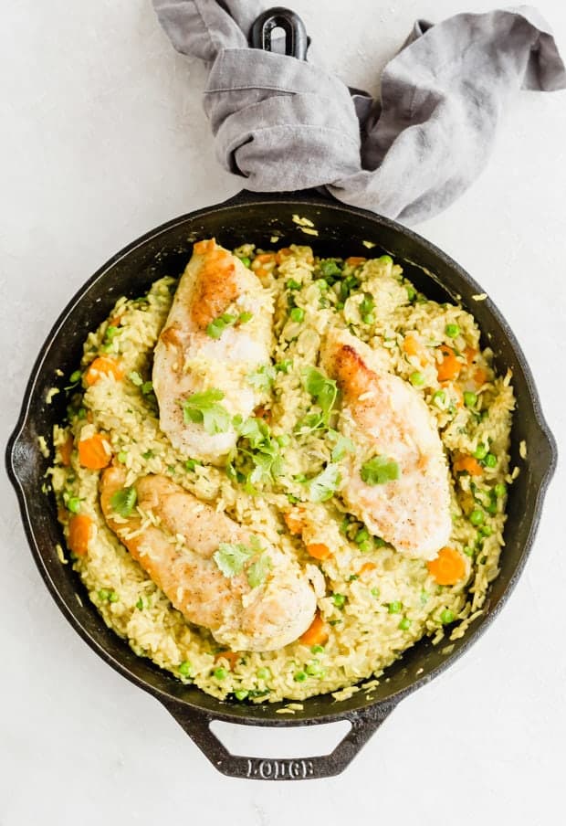 Overhead photo of a cast iron skillet with cooked curry chicken and rice with peas and carrots.