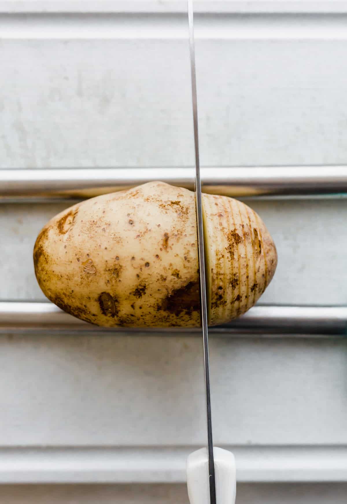 A russet potato with a cutting knife cutting through the potato.