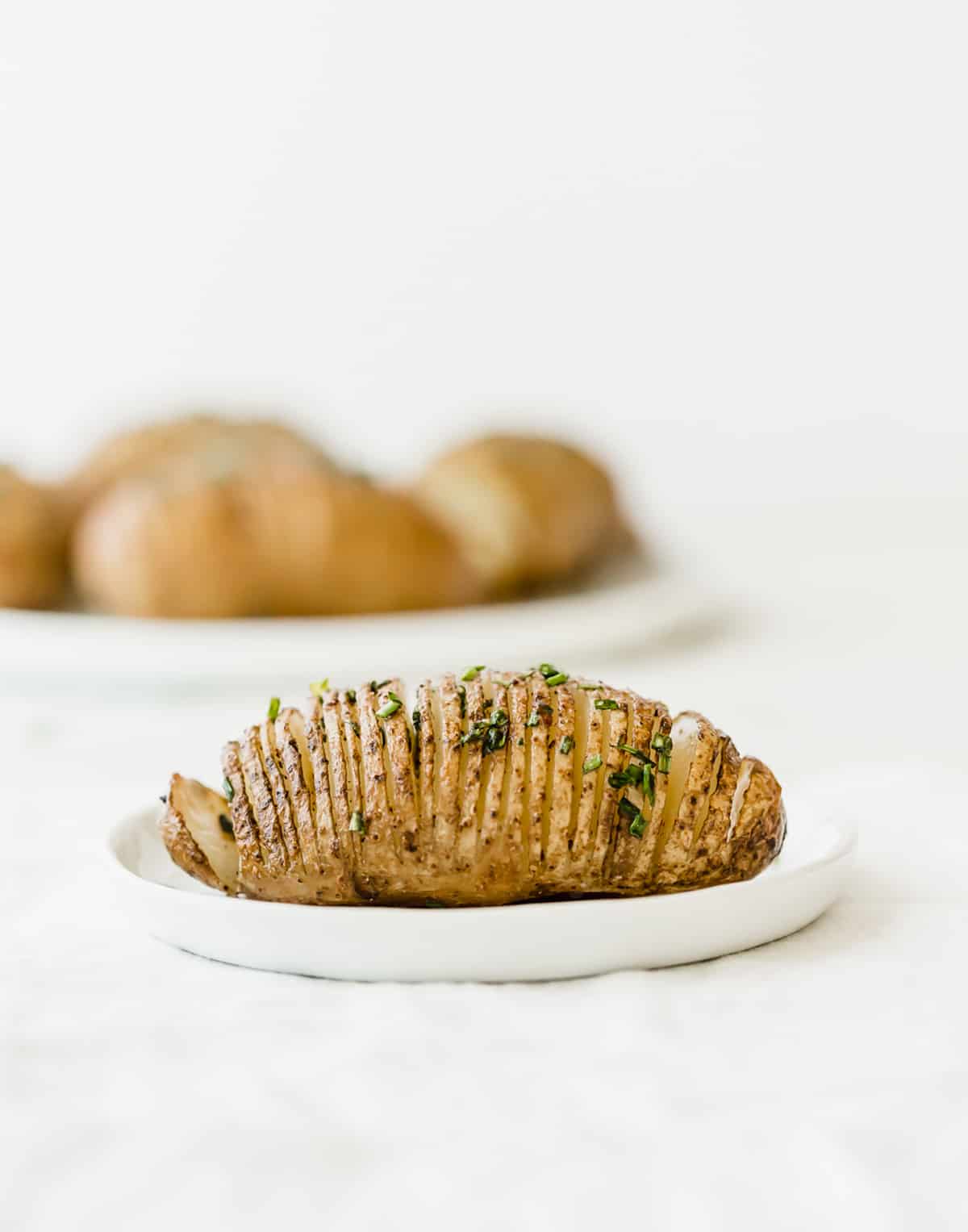 A Hasselback Potatoe on a white plate against a white background.