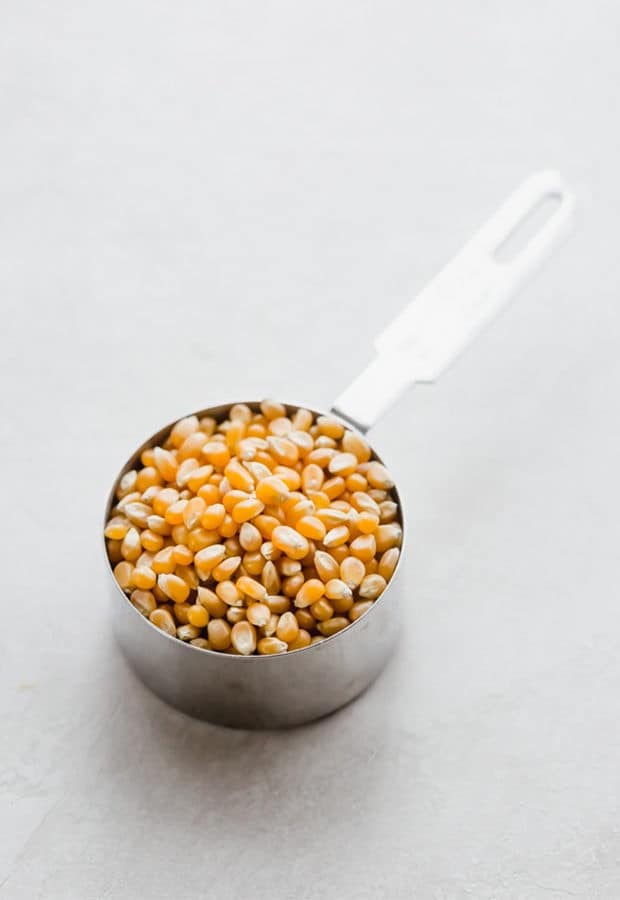 A metal measuring cup full of popcorn kernels.