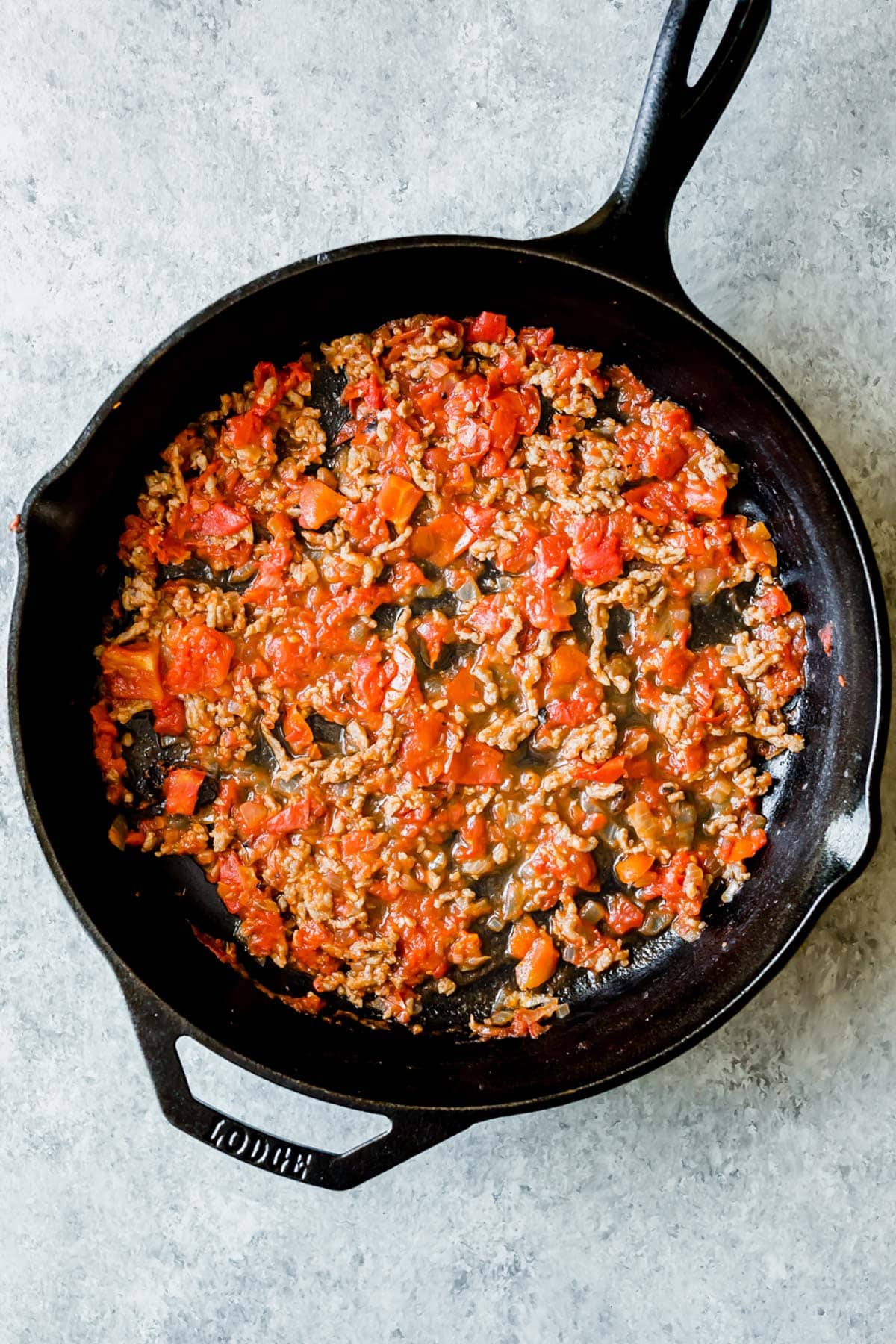 A cast iron skillet with a meat and tomato mixture spread along the bottom.