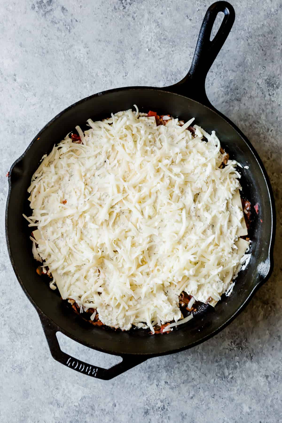 Shredded mozzarella cheese spread overtop of a Cast Iron Lasagna.