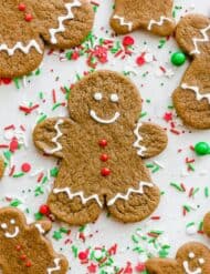 Gingerbread men decorated with white royal icing sitting atop red and green sprinkles.
