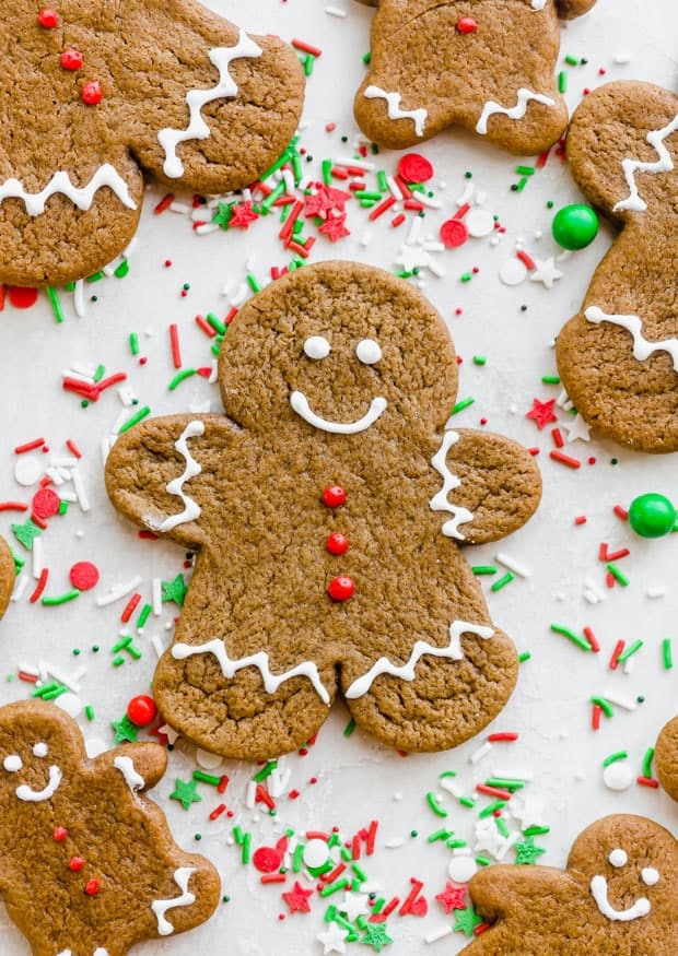 Gingerbread men decorated with white royal icing sitting atop red and green sprinkles.