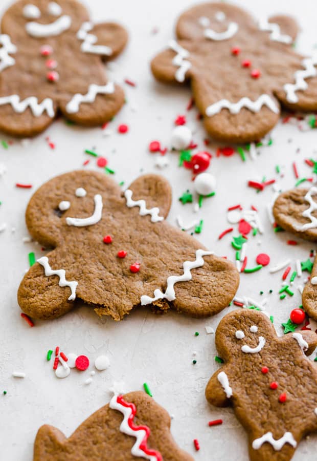 A soft gingerbread cookie man with three red frosting buttons and a bite taken out of the cookies leg.