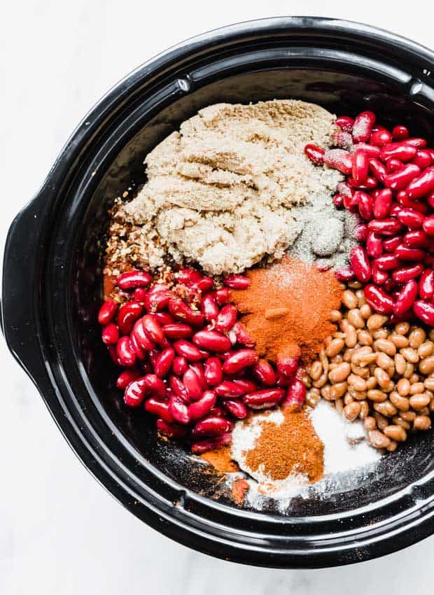 An overhead photo of a black slow cooker full of the ingredients to make sweet and spicy chili.