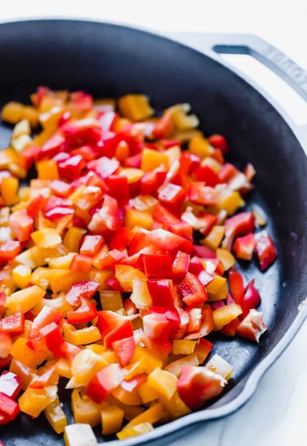 Diced yellow and red peppers in a black skillet in preparation to make sweet and spicy chili.