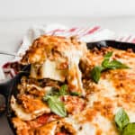 A spoon scooping out Cast Iron lasagna that has been topped with fresh basil.