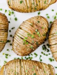 Easy Hasselback Potatoes topped with fresh chives on a white background.