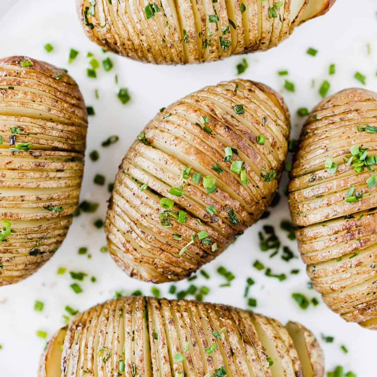 Easy Hasselback Potatoes topped with fresh chives on a white background.