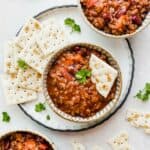 Three bowls of sweet and spicy chili with saltine crackers scattered around the bowls.