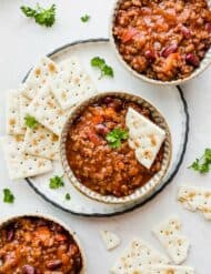 Three bowls of sweet and spicy chili with saltine crackers scattered around the bowls.