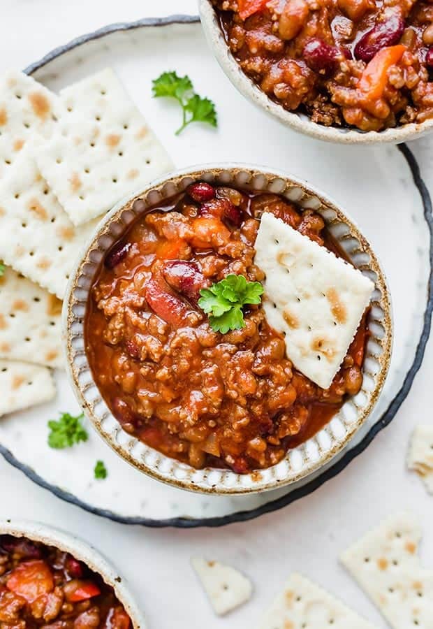 Three bowls of sweet and spicy chili with saltine crackers scattered around the bowls.