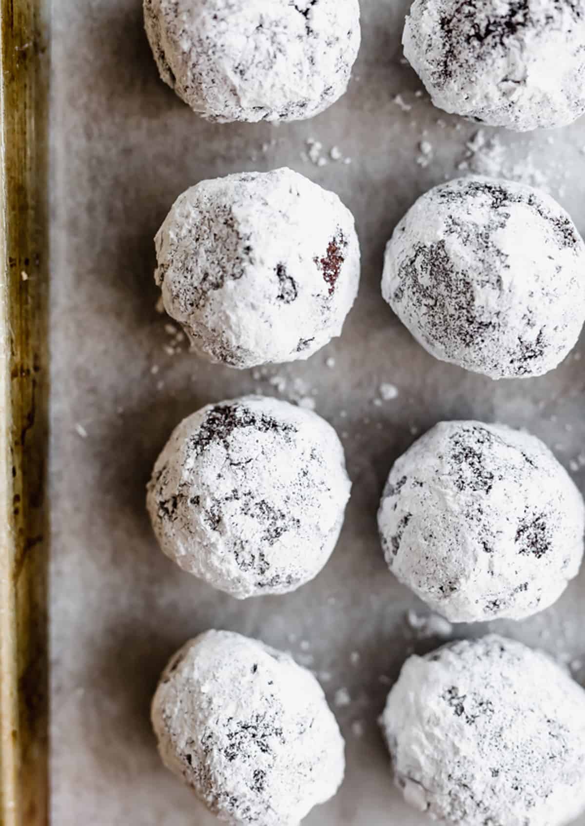 Chocolate Crinkle Cookie dough balls rolled in sugar then powdered sugar, lined up on a baking sheet.