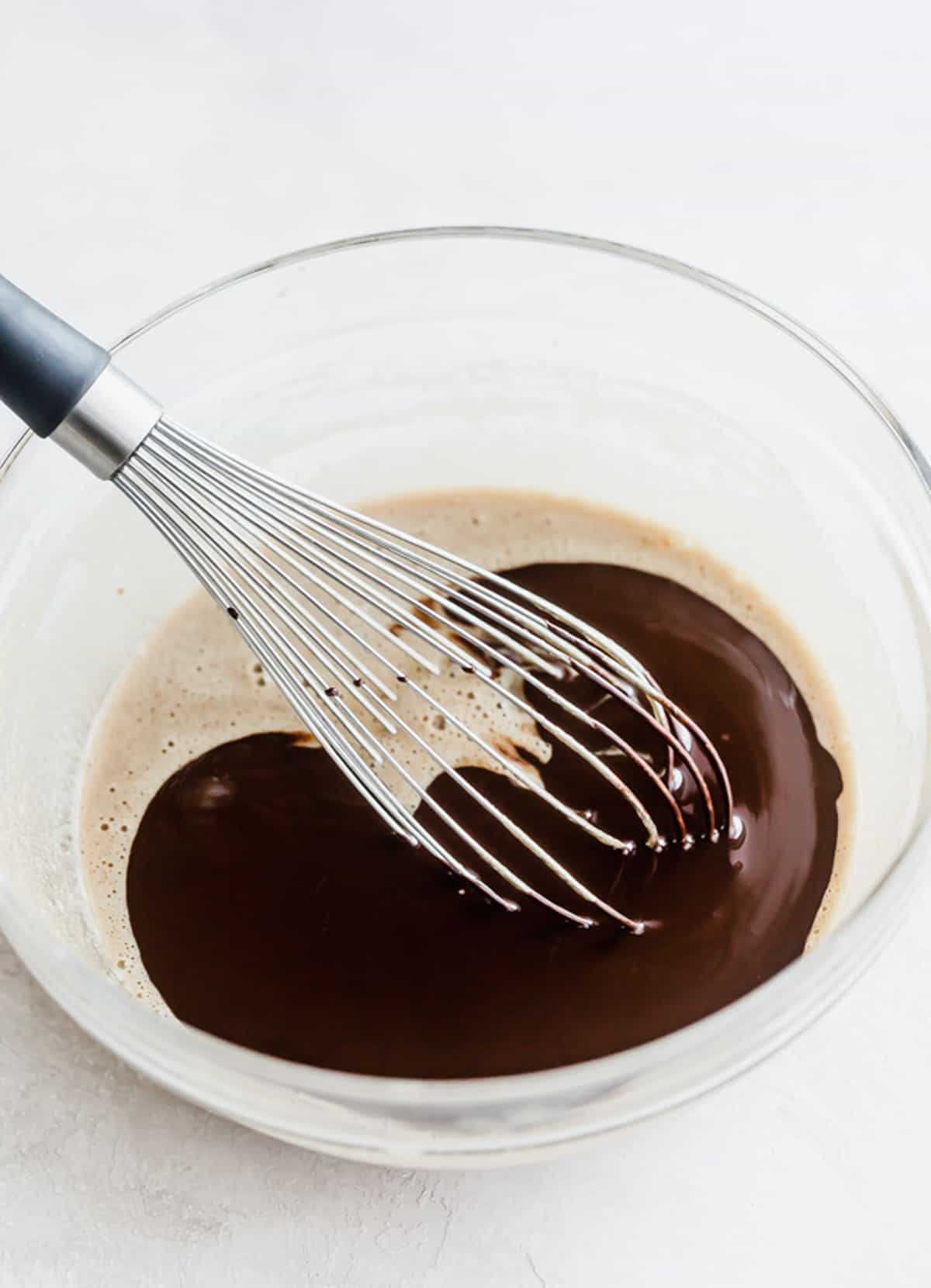 A whisk stirring butter and melted chocolate together.