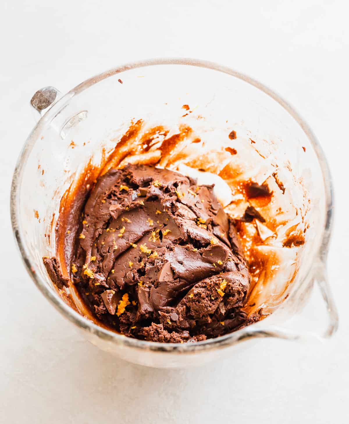 Chocolate Orange Cookie dough made with cream cheese and fresh orange zest in a glass mixing bowl on a white background. 