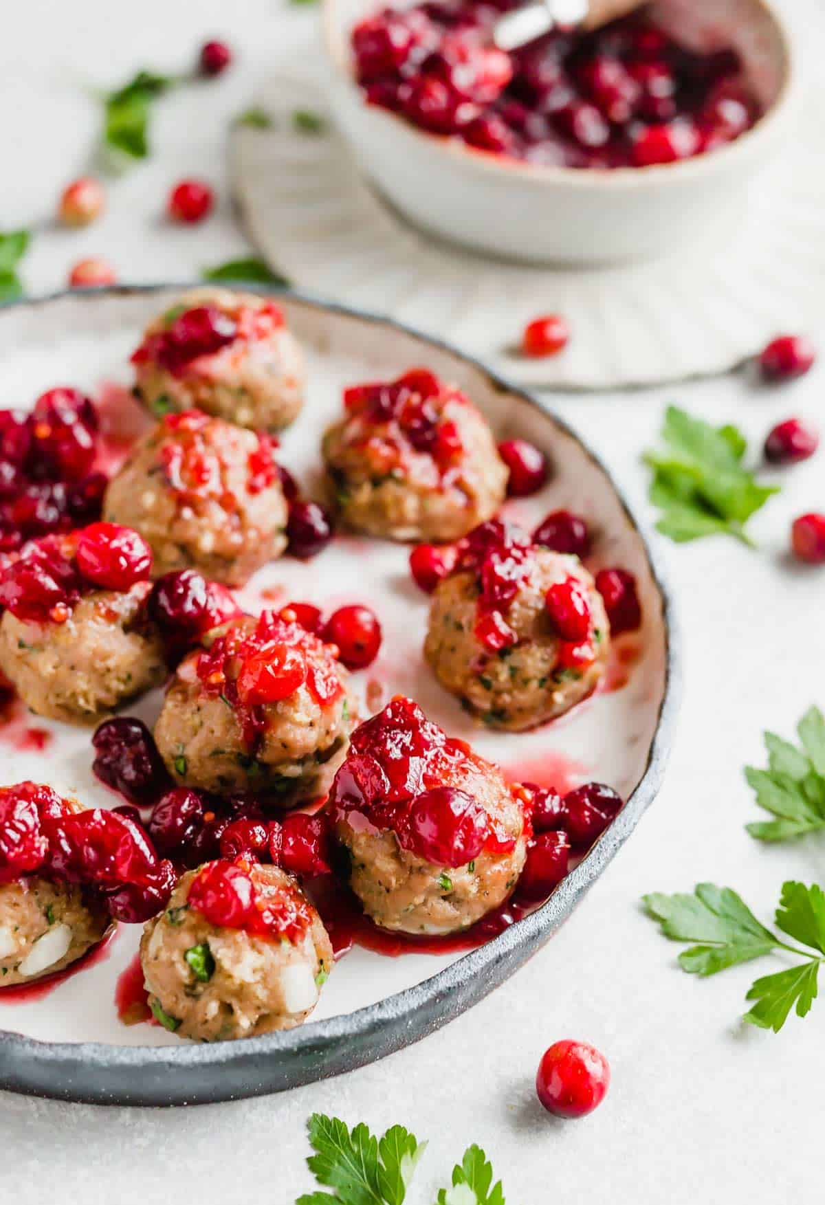 Turkey meatballs topped with cranberry sauce, on a white plate.