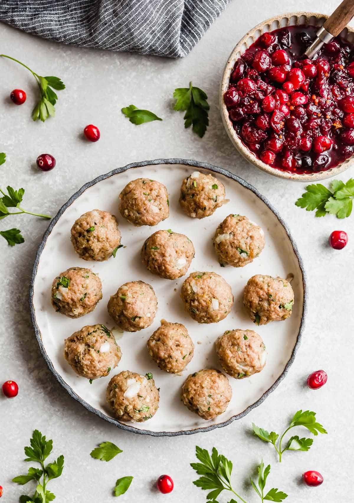 A black rimmed white plate filled with baked turkey meatballs with cranberry chutney in a small bowl to the top right of the plate.