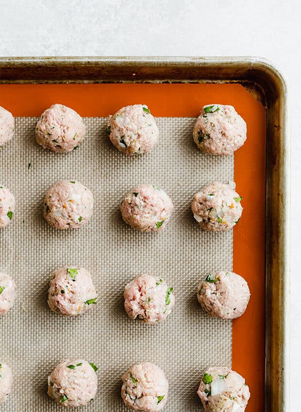 A baking sheet lined with a silicone baking mat and turkey meatballs neatly organized atop the mat.