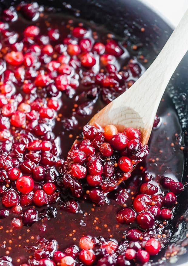Homemade cranberry chutney in a skillet with a wooden spoon scooping up some of the chutney.