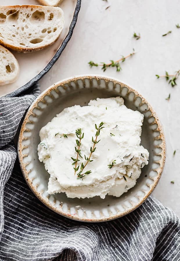 A bowl of whipped goat cheese and cream cheese with a sprig of fresh thyme overtop.