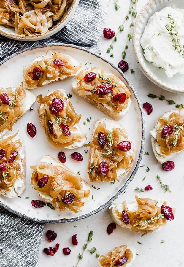 Crostini topped with goat cheese and caramelized onions with a garnish of fresh thyme and dried cranberries.