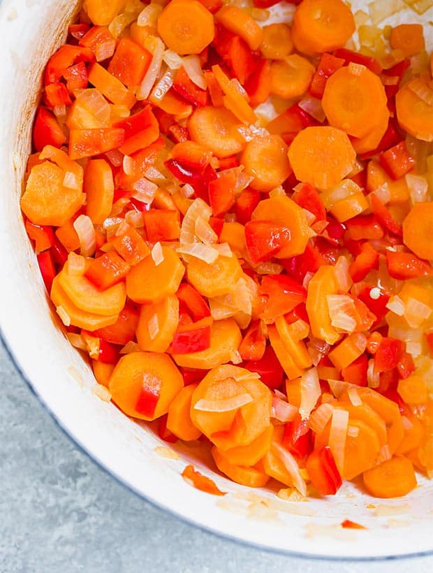 Close up photo of cooked onions, red pepper, and sliced carrots in a dutch oven in preparation to making Massaman curry.