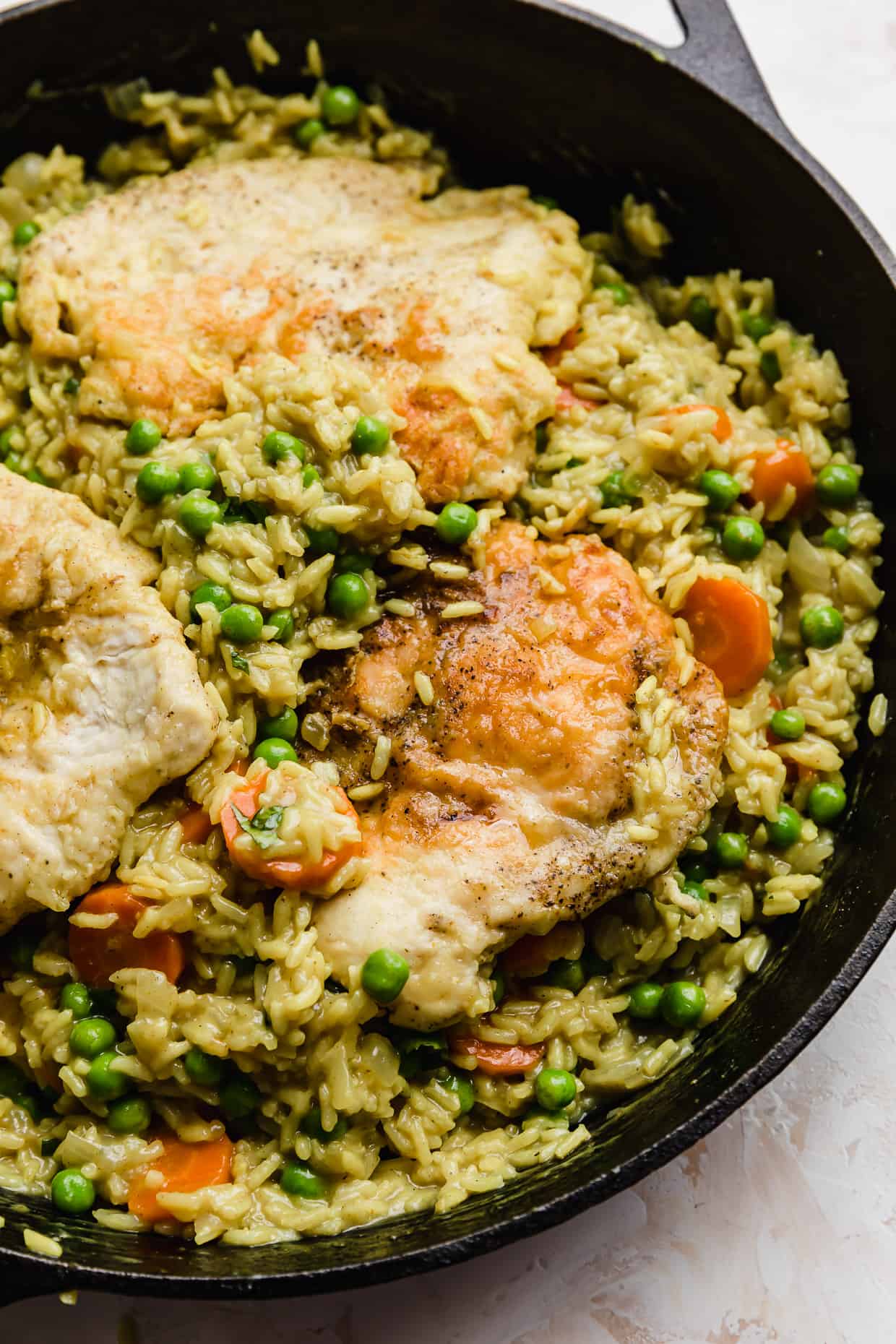 A black skillet with Curry Chicken Rice and Peas and carrots in it.