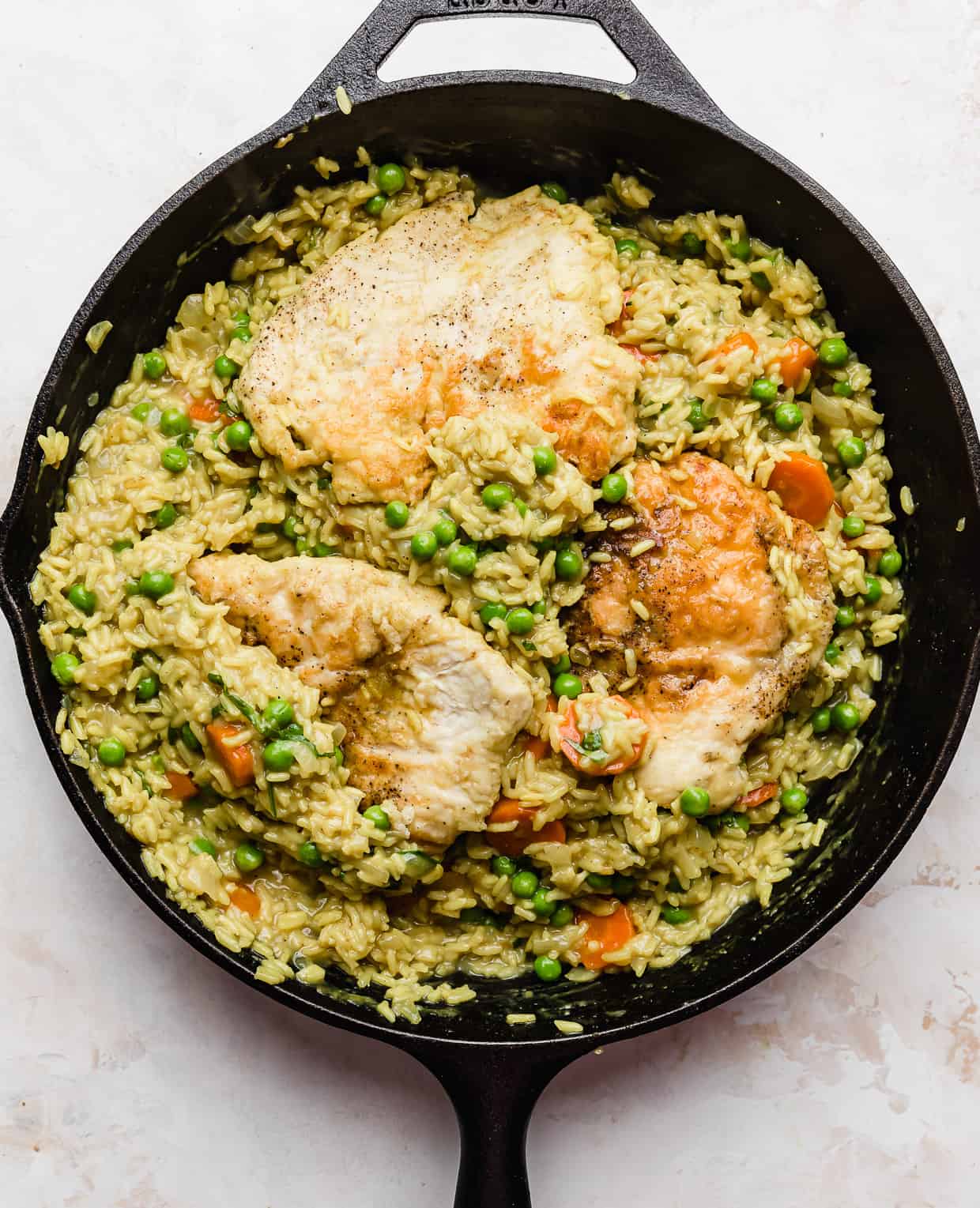 Curry Chicken Rice and Peas and carrots in a black skillet on a white background.