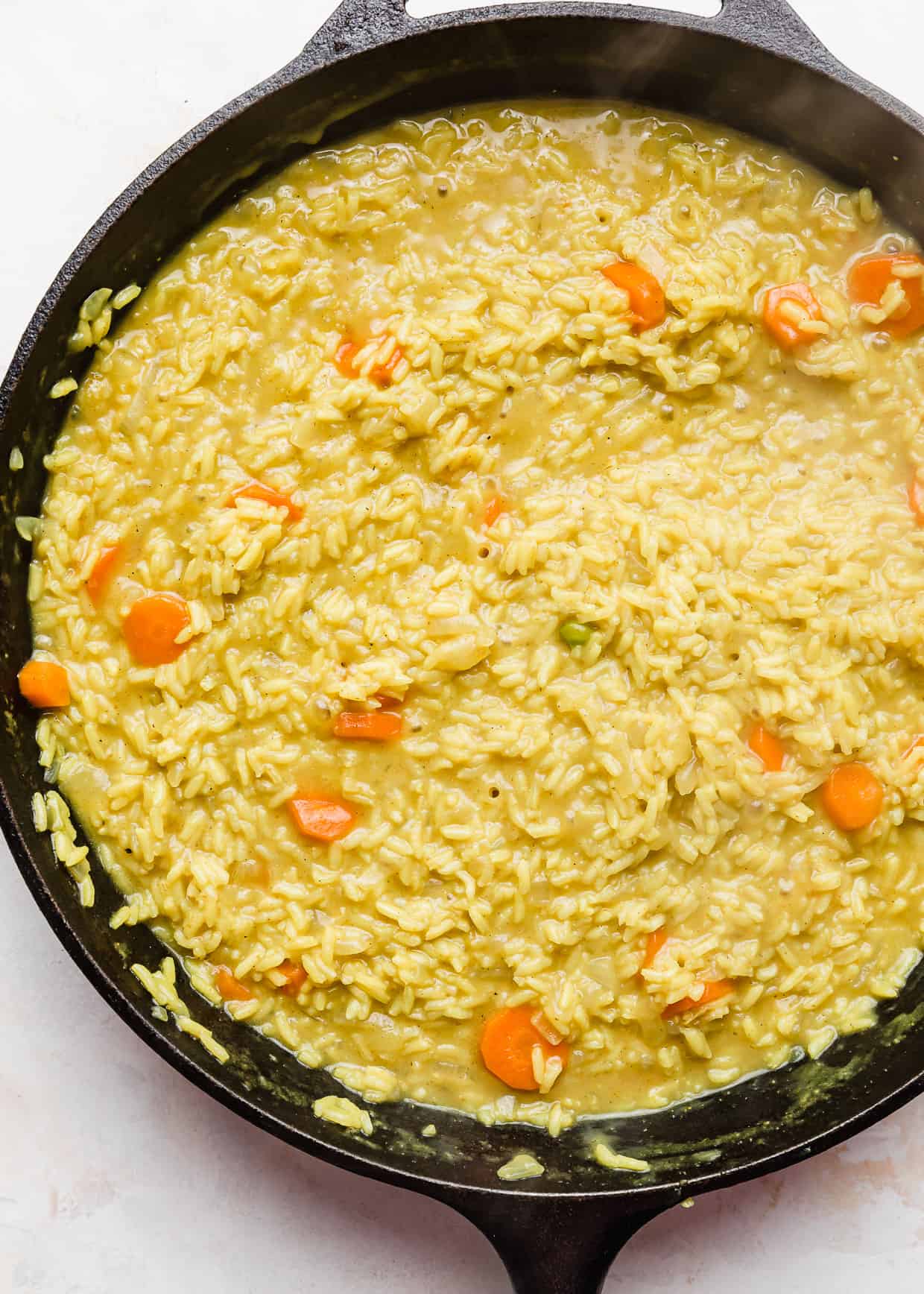 Rice and carrots in a curry rice mixture in a skillet.