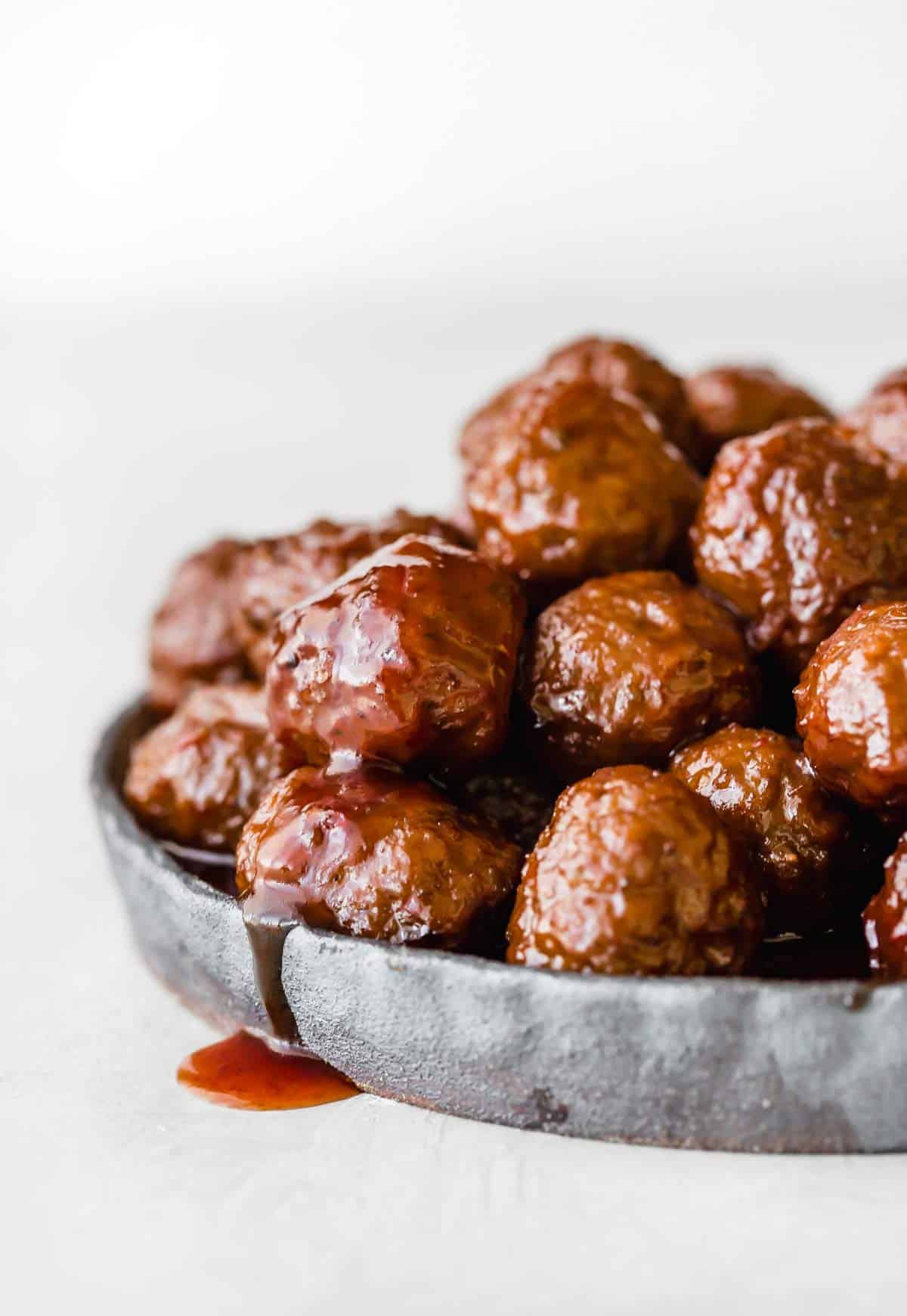 Grape Jelly Meatballs on a black plate against a white background.