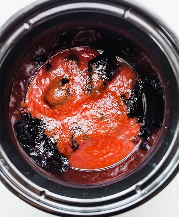 A black crockpot with grape jelly and chili sauce in it.