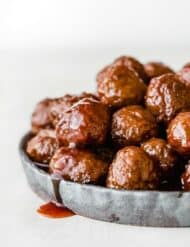 Grape jelly bbq meatballs on a black rimmed plate with sauce drizzling over the side of the plate.