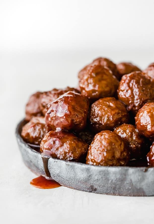 Grape jelly bbq meatballs on a black rimmed plate with sauce drizzling over the side of the plate.