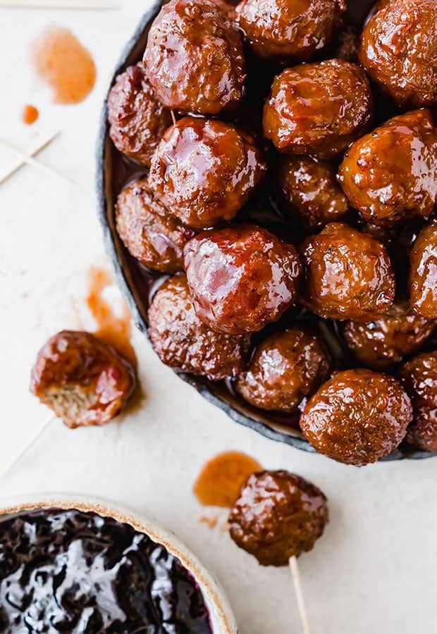 Overhead photo of grape jelly meatballs stacked on a plate, with a bowl of grape jelly to the side.