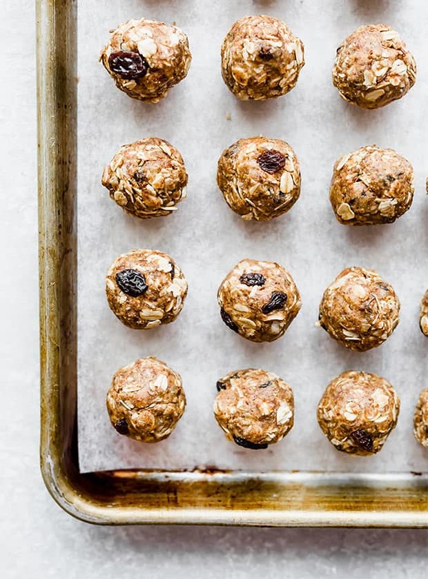 A parchment lined baking sheet with small rolled balls of oatmeal raisin energy bites in a row. 