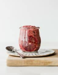 A straight on photo of a glass jar full of blood orange chia pudding sitting on top of a plate and wooden cutting board.