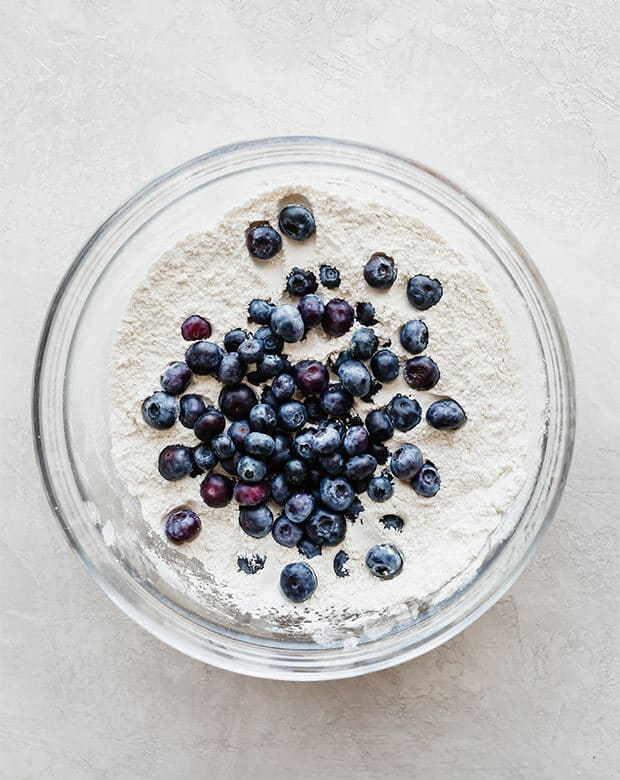 Glass bowl with dry ingredients and fresh blueberries for making easy blueberry muffins.