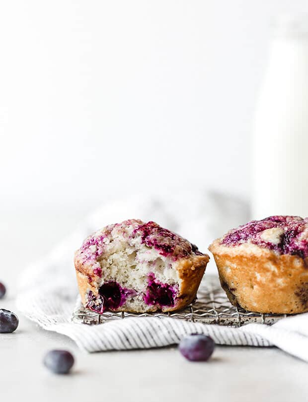 Two blueberry muffins side by side, with one muffin having a bite taken out of it, exposing fresh blueberries baked into the muffin.