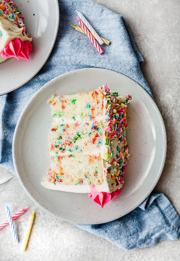 A slice of a layered Funfetti Cake, with birthday candles scattered around the cake slice.