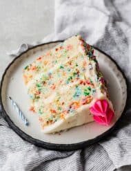 A slice of funfetti cake laying on its side on a black border lined plate.