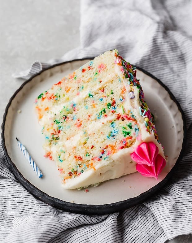 A slice of funfetti cake laying on its side on a black border lined plate. 